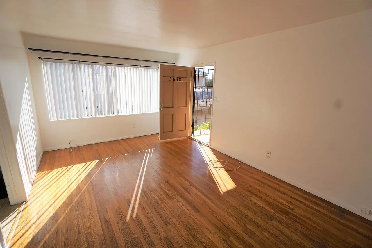 Sun-filled living room with hardwood-style floors and a large picture window — Ocean Beach, San Diego